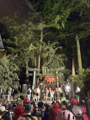 深夜の神社で鳥居前に集う夜間登山挑戦者と祭礼の様子