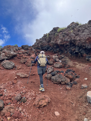 男体山の赤茶色の火山岩が広がる登山道を、登山者が山頂へ向かって登る様子